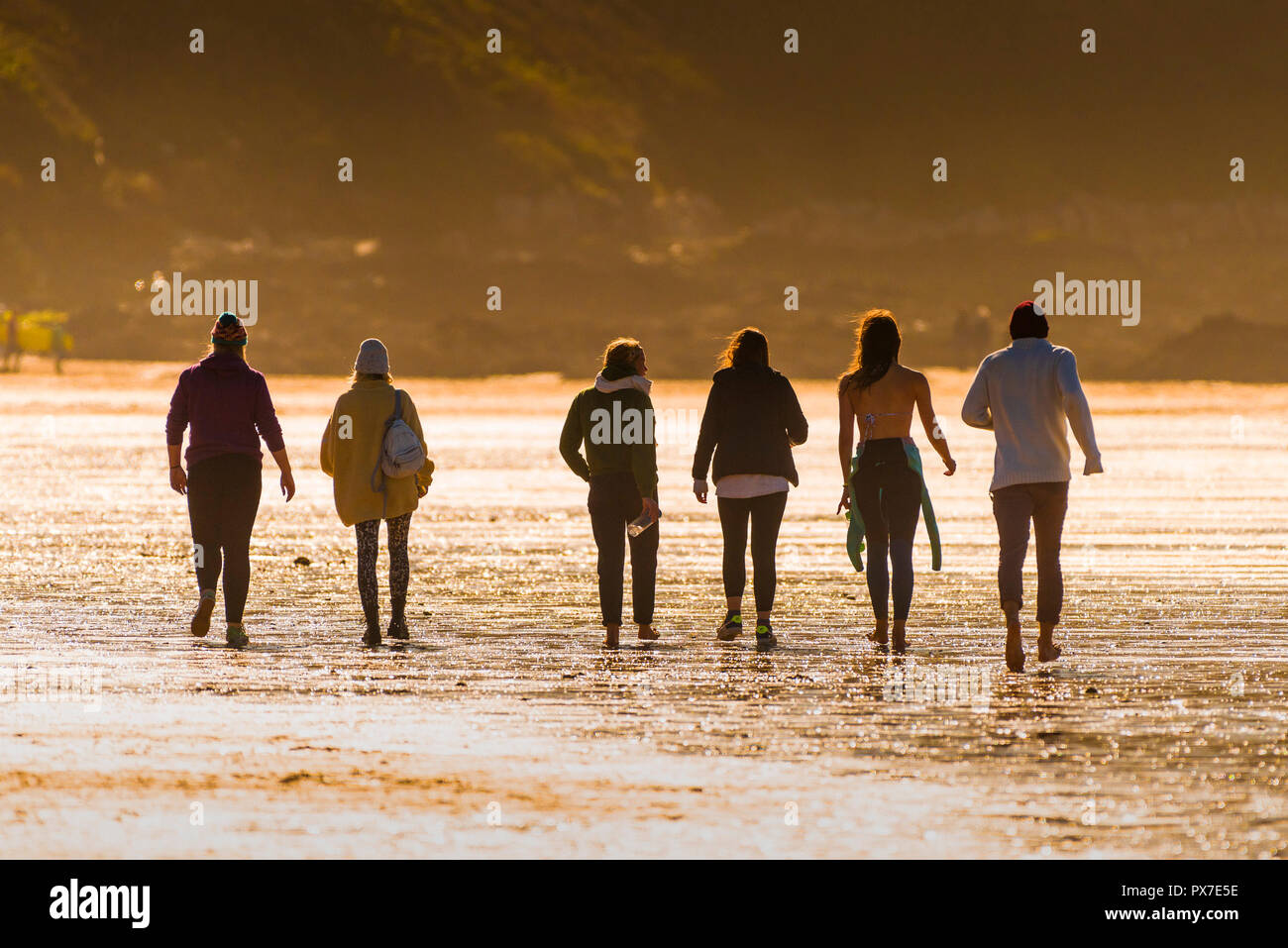 Un gruppo di persone che camminano attraverso Fistral Beach durante la luce della sera. Foto Stock