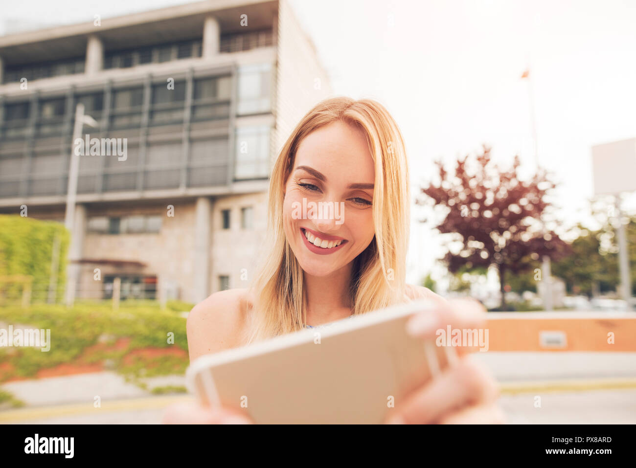 Bella giovane donna è l'utilizzo di un'app nel suo smart phone dispositivo per la riproduzione di un gioco, mentre all'aperto Foto Stock