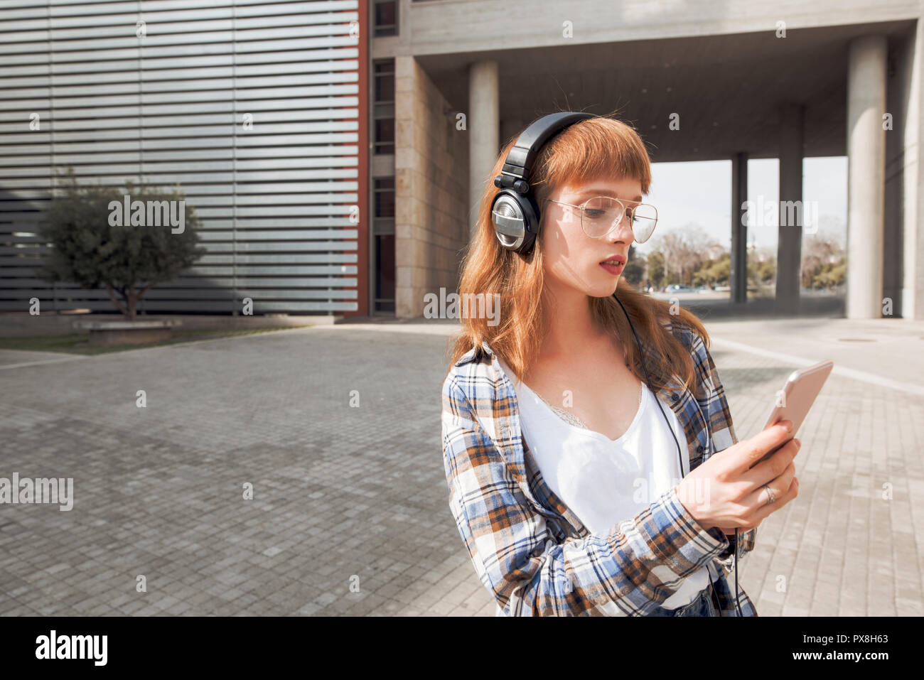 Un giovane hipster donna con i capelli rossi, utilizza un'applicazione nel suo smart phone dispositivo per inviare un messaggio di testo e ascoltare musica Foto Stock
