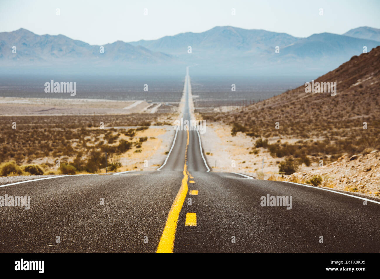 Classic vista panorama di un interminabile dritta strada che corre attraverso il paesaggio arido del sud-ovest americano con estremo calore haze in estate Foto Stock