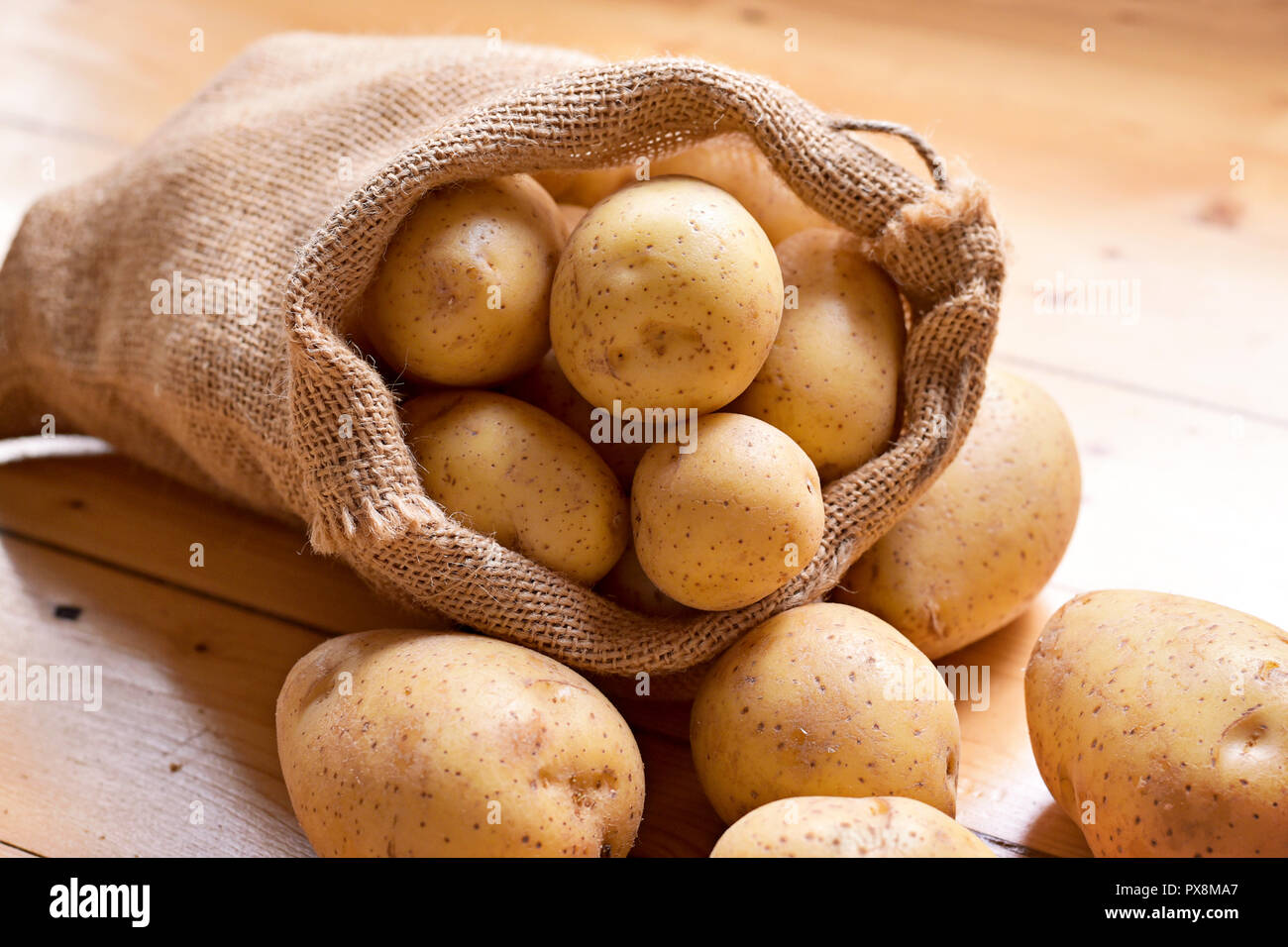 Crudo fresco patate in un sacco di tela. Terrosa scena di patate con cilicio, la disposizione su un sfondo di legno, ingrediente di cottura. Foto Stock