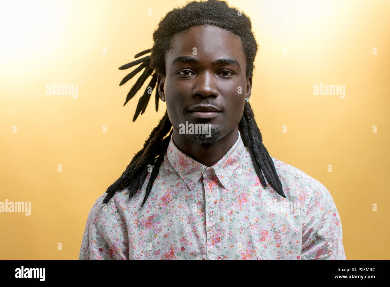 Bel giovane uomo africano indossando fiori shirt contro sfondo giallo Foto Stock