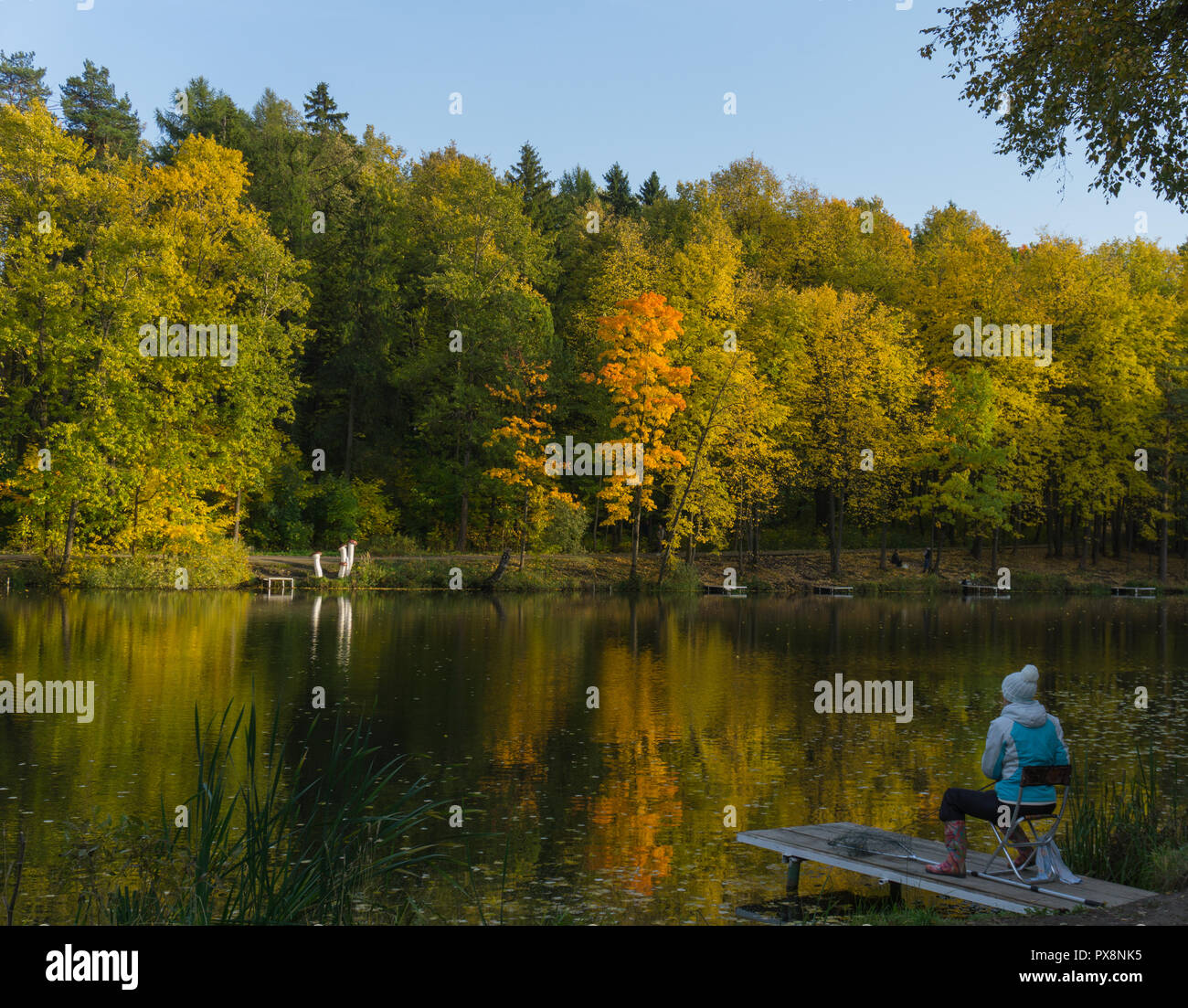 Ragazza di pesca al lago, Giallo autunno alberi riflesso sull'acqua Foto Stock