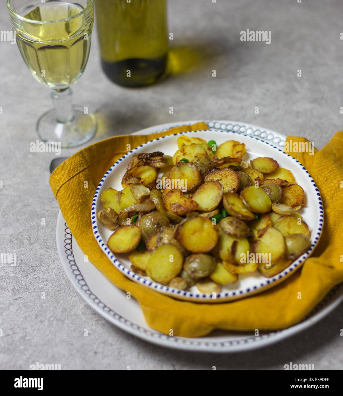 Impostazione tabella per le vacanze la cena. Patate fritte con funghi e cipolla a sfondo chiaro. Giallo igienico, vetro e una bottiglia di vino bianco vicino a. Foto Stock