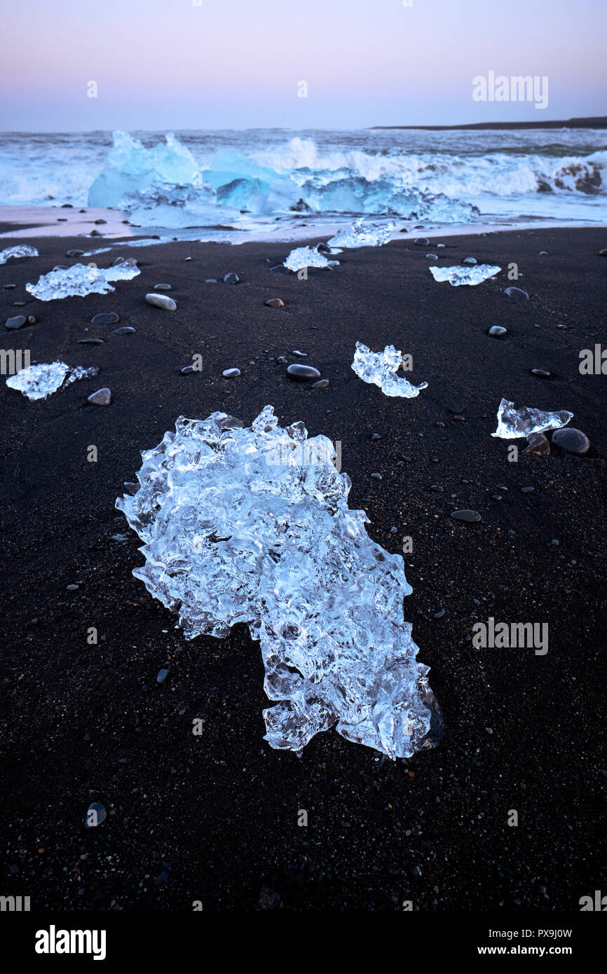 La fusione lavato fino iceberg i frammenti in basalto nero alla spiaggia di sabbia di Jokulsarlon nel sud dell'Islanda. Foto Stock
