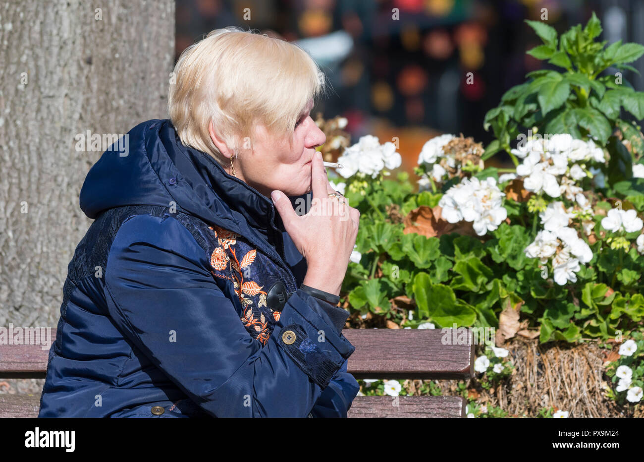 Vista laterale di una donna caucasica di mezza età seduta a fumare una sigaretta arrotolante nel Regno Unito. Foto Stock