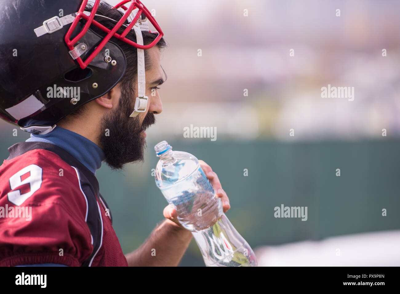 Stanco di un giocatore di football americano di acqua potabile durante il riposo dopo il duro allenamento nel campo Foto Stock
