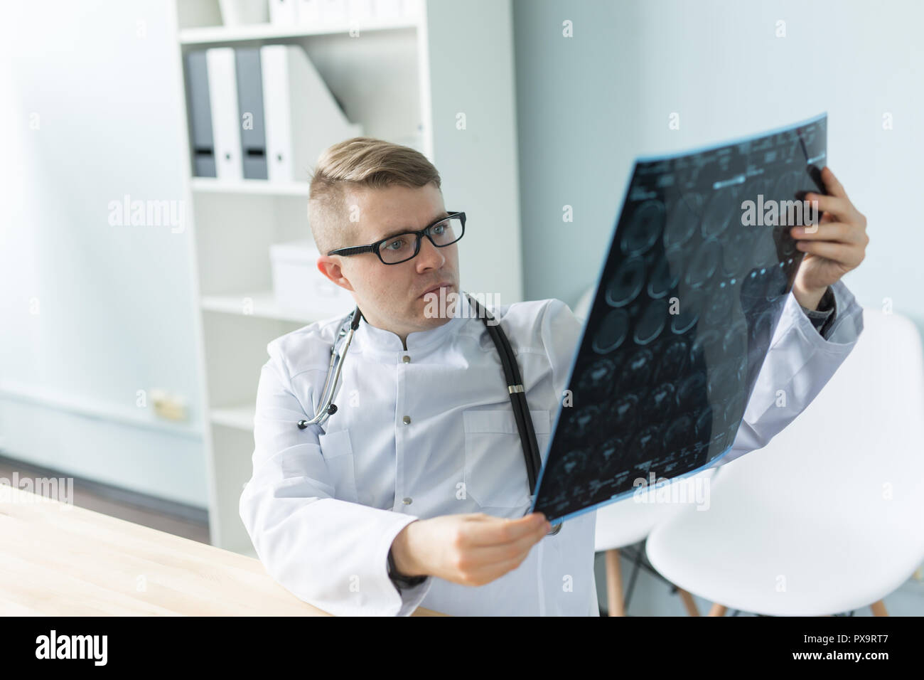 Giovane medico caucasica seduta nel suo ufficio e alla ricerca di immagini a raggi X Foto Stock