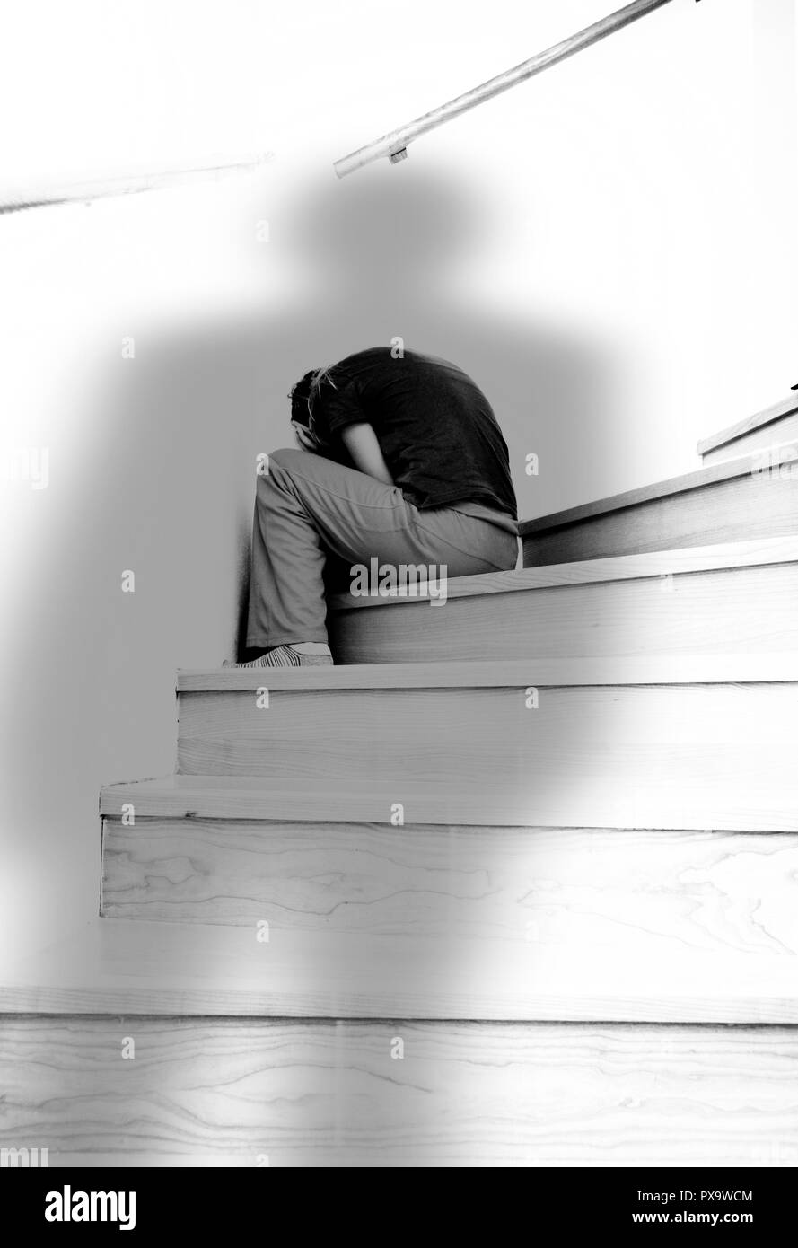 Ragazza seduta sul gradino e nascondendo il suo viso nella paura, ombra minacciosa di un uomo al di sopra di lei, abuso domestico concept Foto Stock