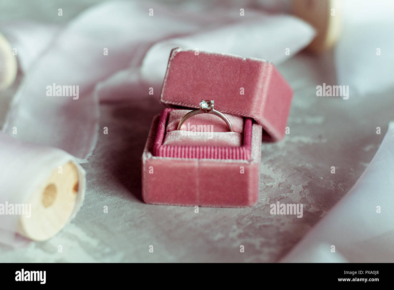 Romantico presente: rosa scatola di velluto con un anello di nozze e luce nastri di raso su sfondo grigio Foto Stock