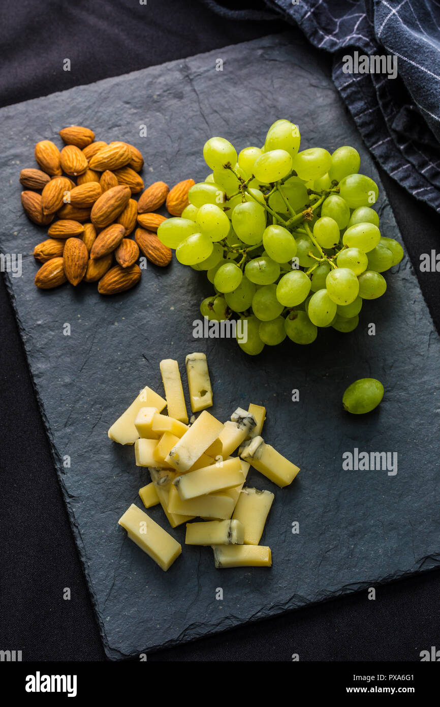 Pezzi di formaggio di uva succosa e noci sulla scheda di ardesia. Foto Stock