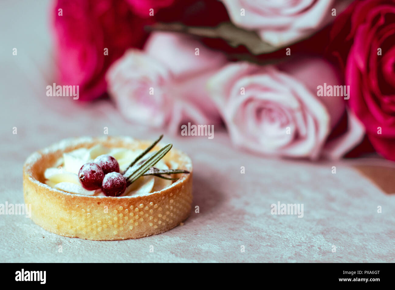 Offerta regalo romantico: dolci con panna e frutti di bosco e un bouquet di rose rosa su sfondo chiaro Foto Stock
