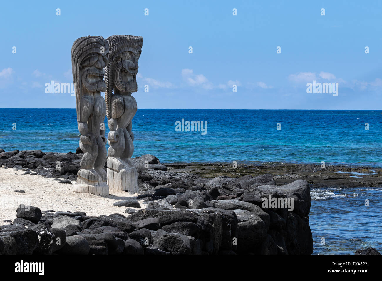 Coppia di stato in legno (Tikis), luogo di rifugio (Honaunau), Hawaii. In piedi sulla sabbia bianca, accanto alla parete barriera di nera lava rock. Foto Stock