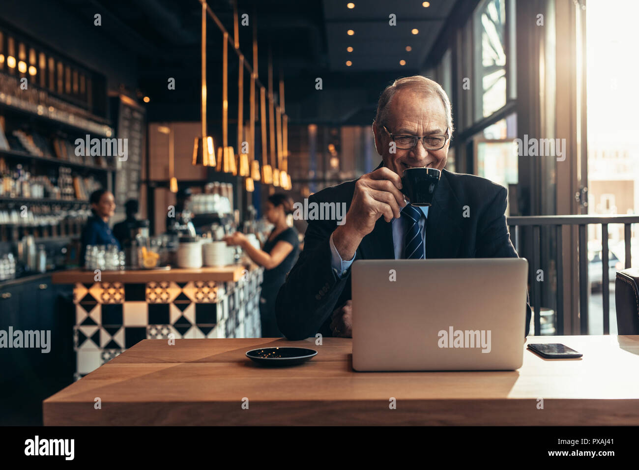 Sorridente imprenditore senior seduti al bar a bere una tazza di caffè e guardando il laptop. Imprenditore maschio presso la caffetteria con il computer portatile. Foto Stock