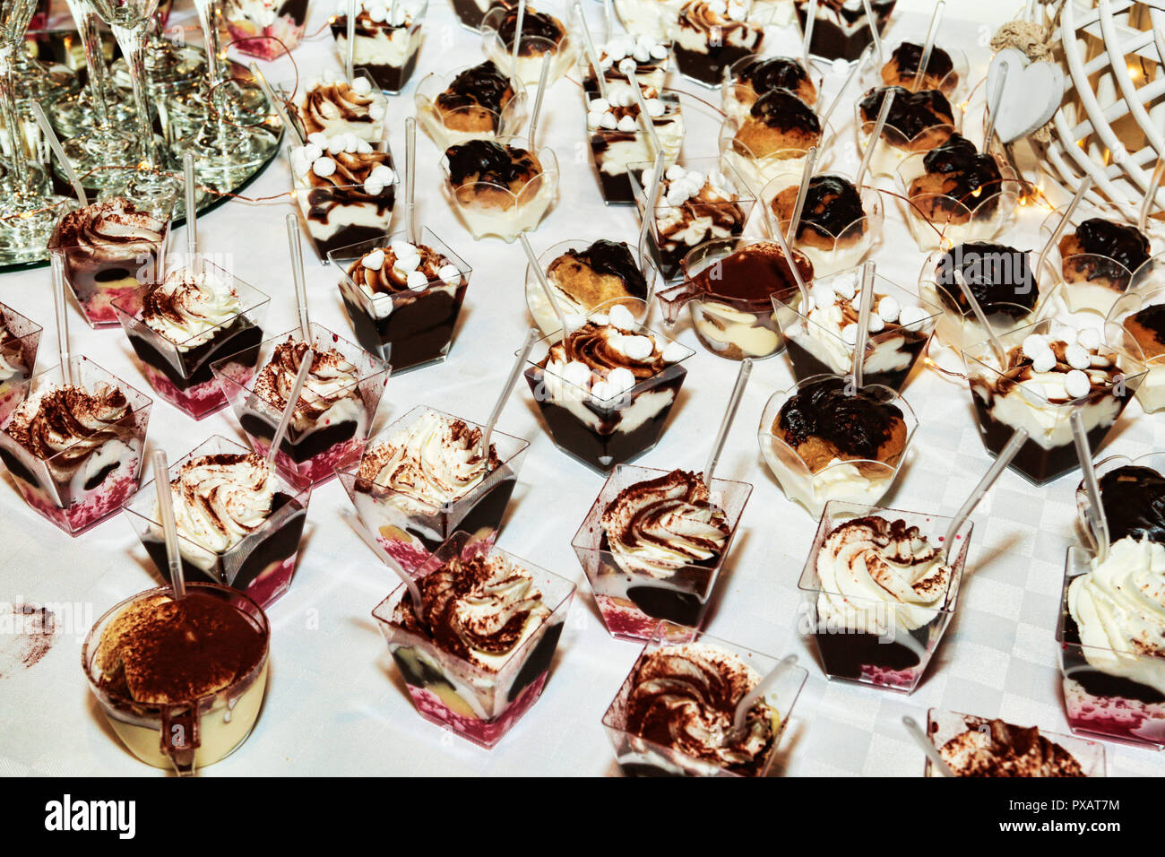 Molte tazze con diversi tipi di dessert basato su mousse e panna cotta guarnita con cioccolato e crema di panna Foto Stock