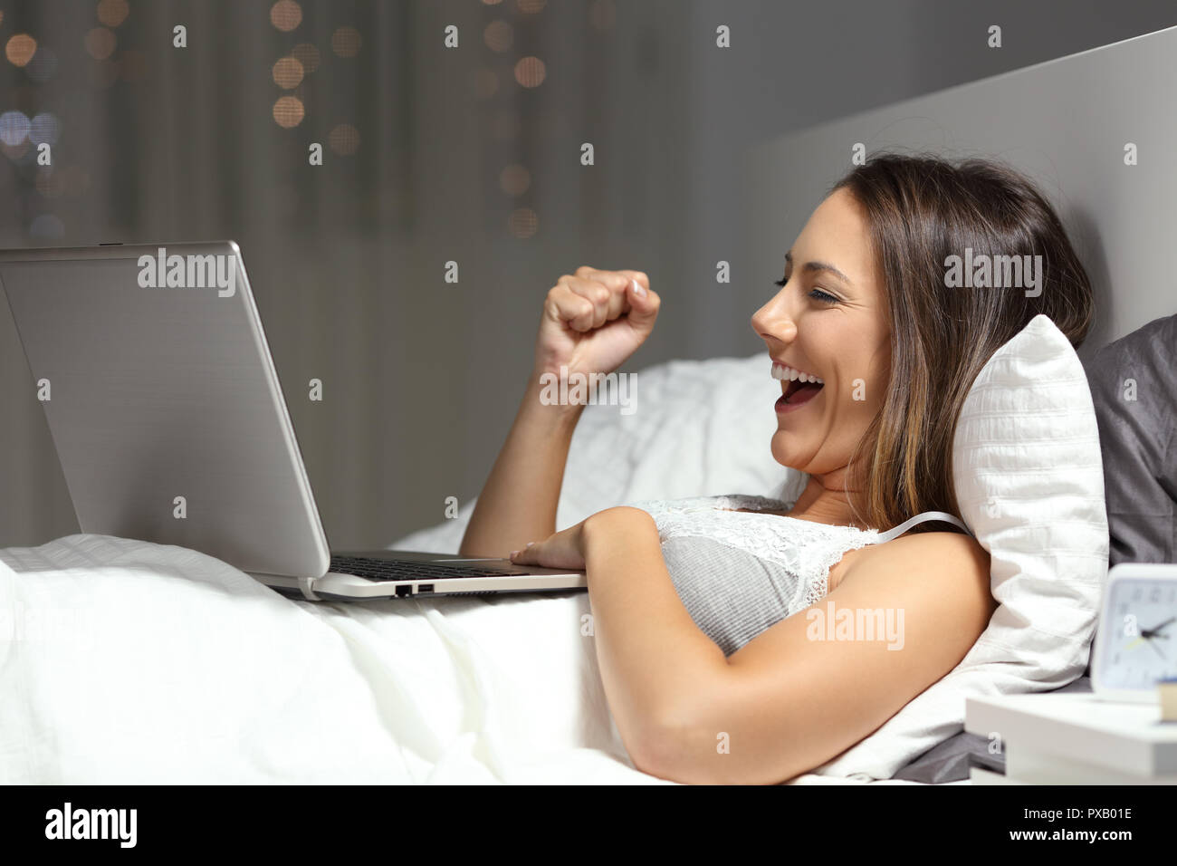 Vista laterale ritratto di una donna entusiasta celebrare la buona notizia online sul letto nella notte a casa Foto Stock