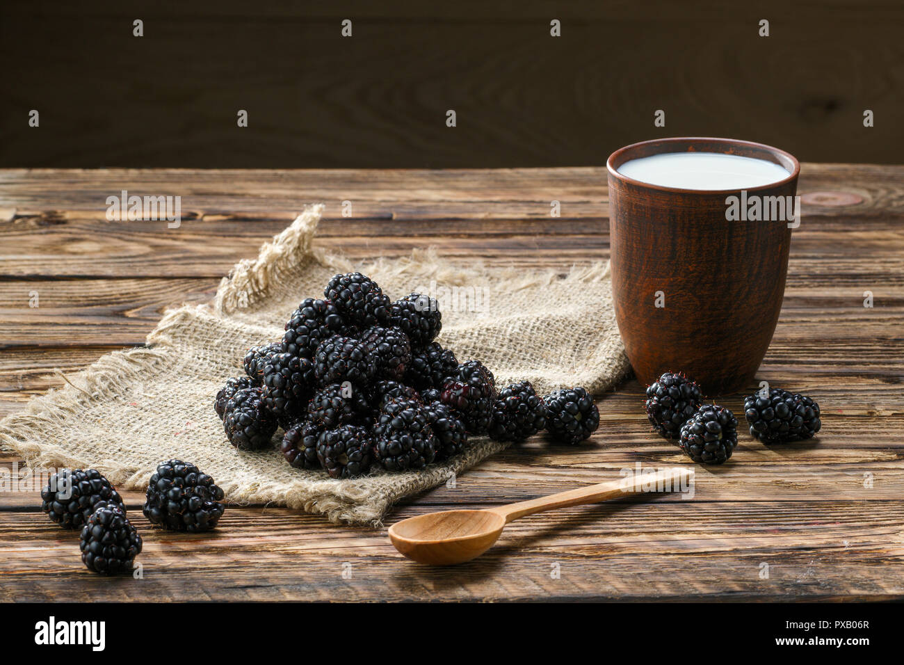 Cumulo di dewberry fresca su un letto di sacco table-igienico e tazza di argilla con il latte sul tavolo di legno Foto Stock