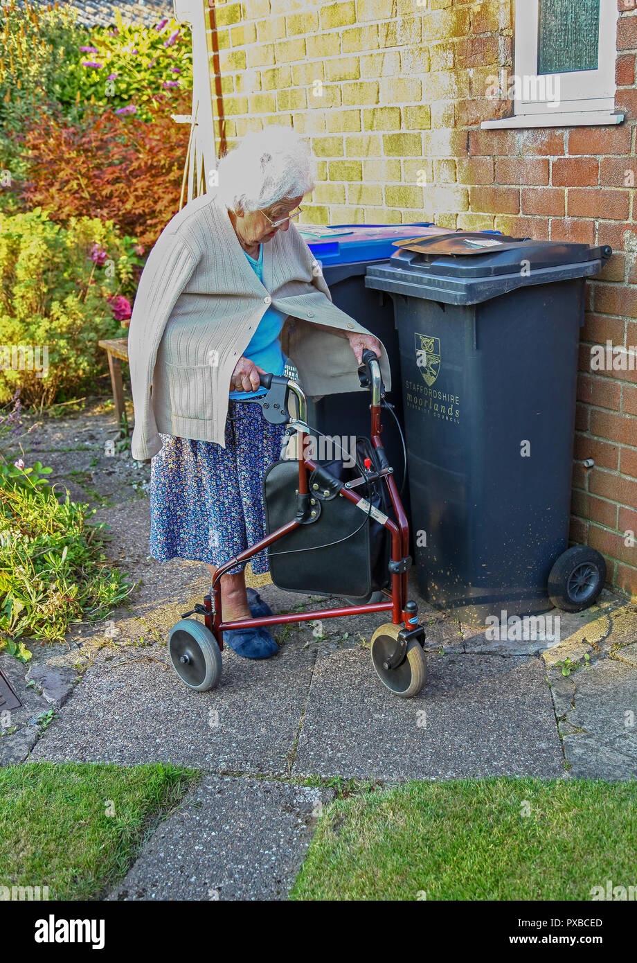 Una donna anziana camminare con l'aiuto di un trike, 3 passeggino con ruote, 3 ruota aiuti a piedi o 3 ruota Walker, England, Regno Unito Foto Stock