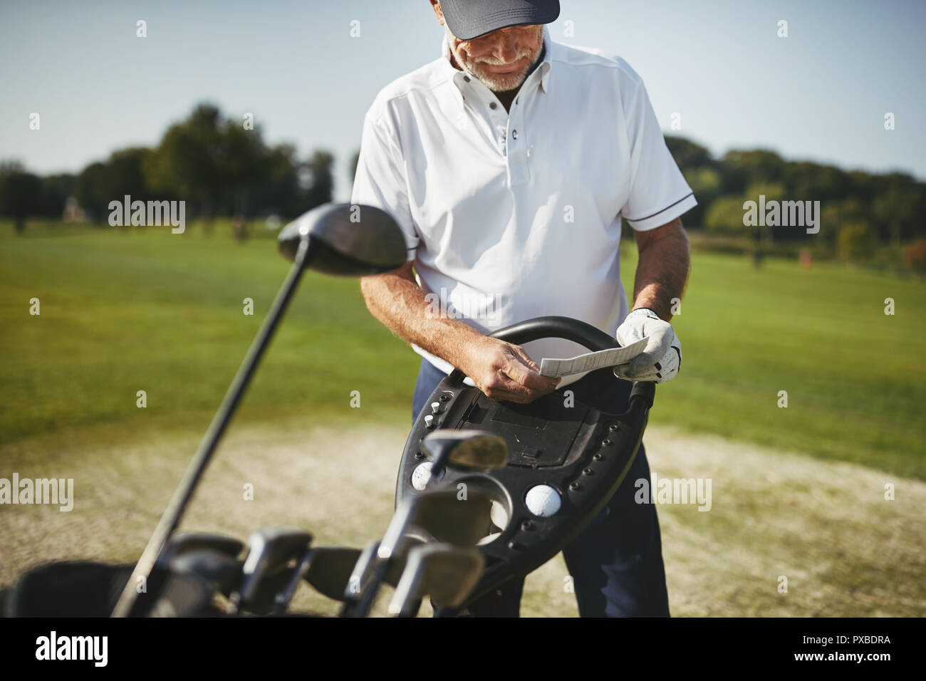 Senior sportivo uomo in piedi dal suo club e la lettura del suo scorecard mentre godendo di un round di golf in una giornata di sole Foto Stock