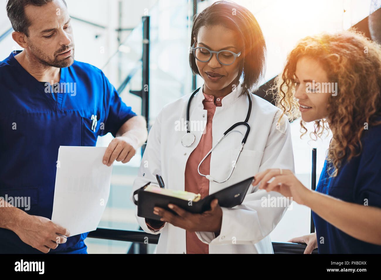 Diversi gruppi di giovani medici in piedi insieme in un corridoio di ospedale a discutere di un paziente la diagnosi Foto Stock