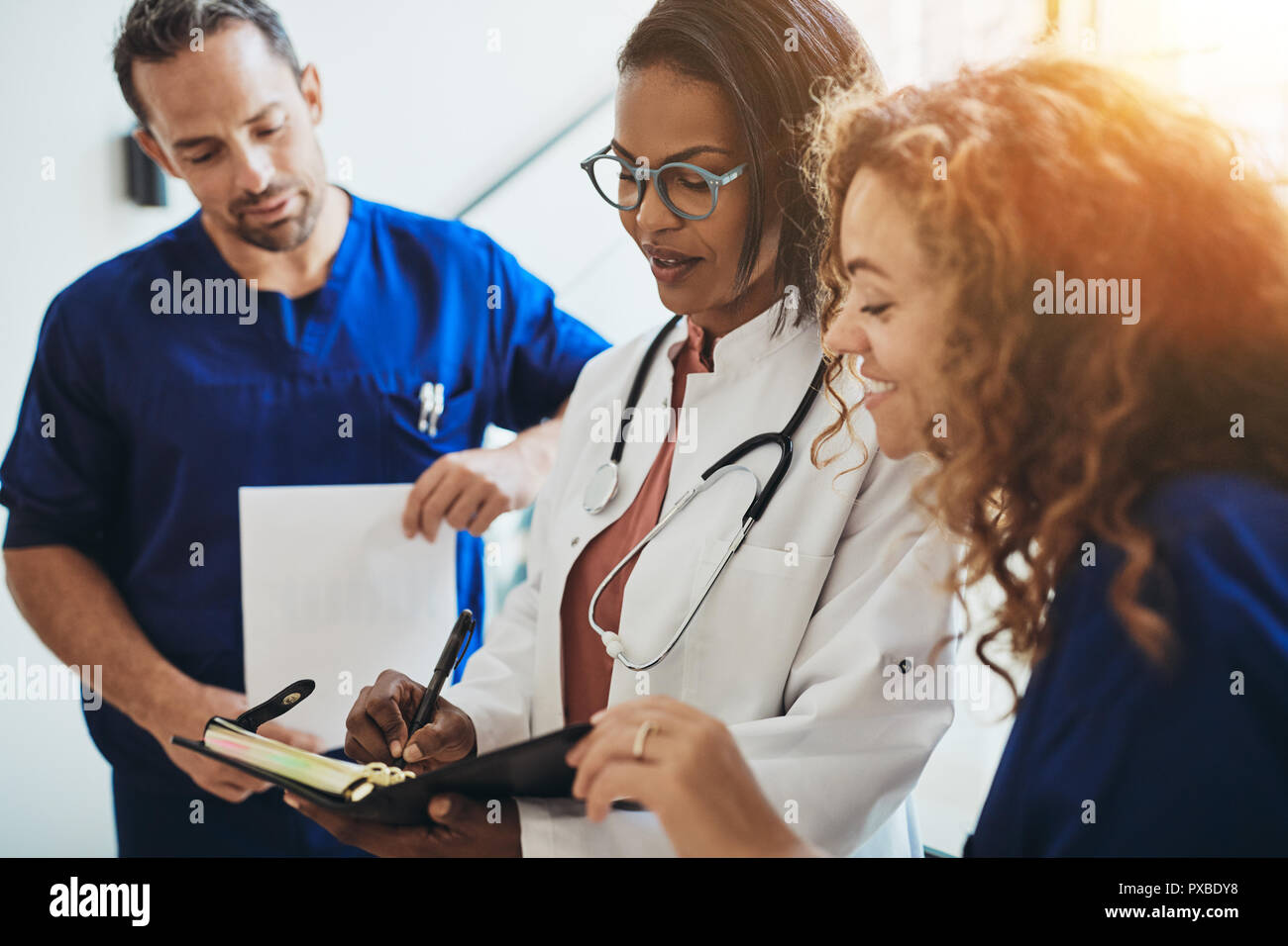 Diversi gruppi di giovani medici in piedi in un corridoio di ospedale a discutere di un paziente's dignosis Foto Stock