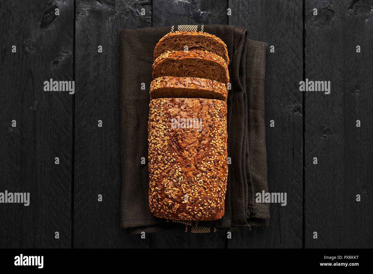 Focaccia di fettine di pane integrale su asciugamano scuro su tavoli in legno nero. Vista da sopra con copia spazio. Foto Stock