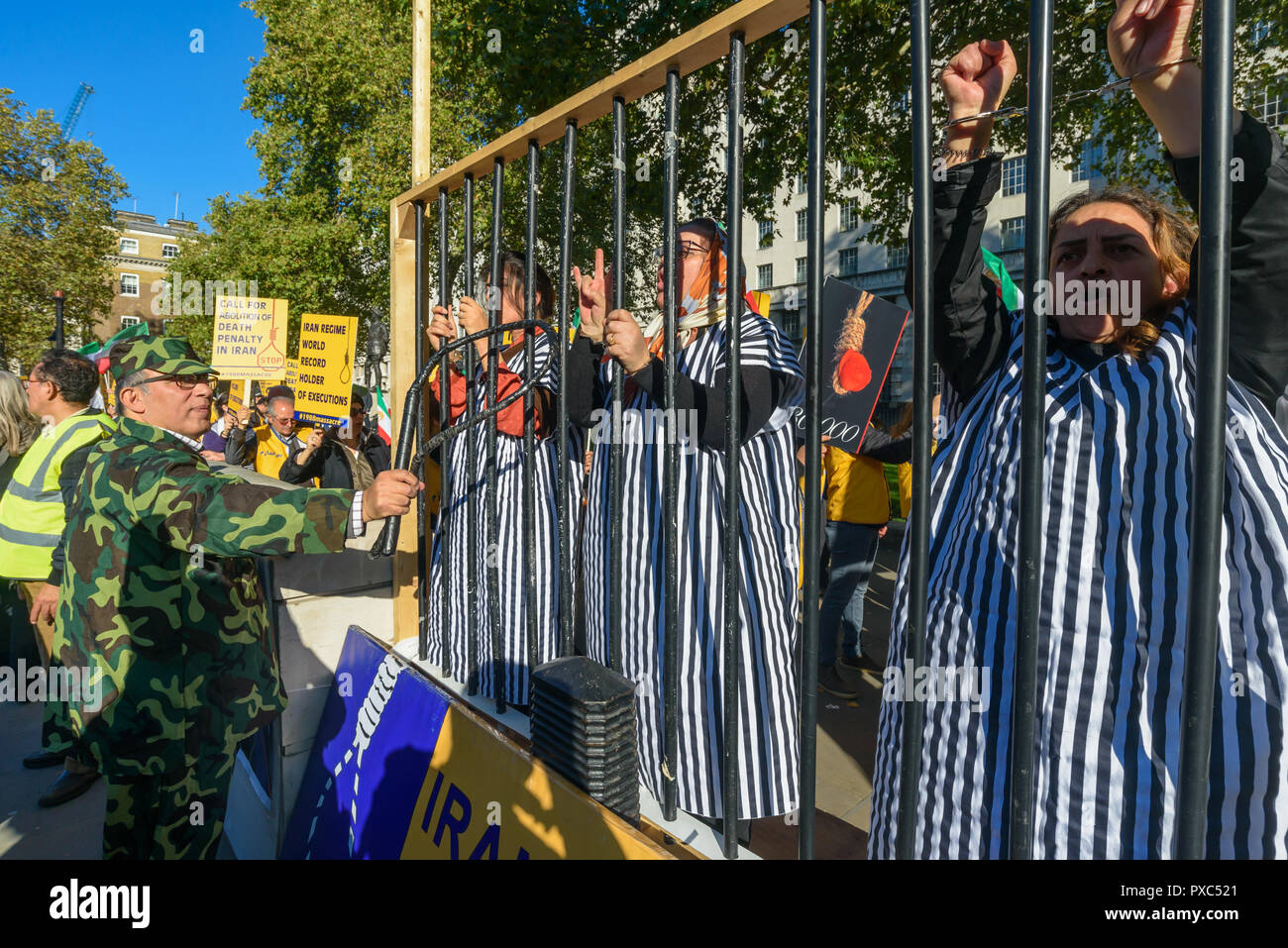 Londra, Regno Unito. 20 ott 2018. Le donne in abito da prioni stand dietro prigione barre mentre un uomo li minaccia con una frusta alla protesta. Dietro un banner "democrazia in Iran con Maryam Rajavi', Mujaheddin del popolo dell'Iran terrà una manifestazione di protesta contro la repressione del regime attuale in Iran con un patibolo e tre donne detenute in una cella di prigione che illustra il regno del terrore vi e per chiedere la fine delle esecuzioni ci, . Rajavi, il leader dell'OMPI, ha esposto un 10-punto manifesto chiamando per un Credito: ZUMA Press, Inc./Alamy Live News Foto Stock