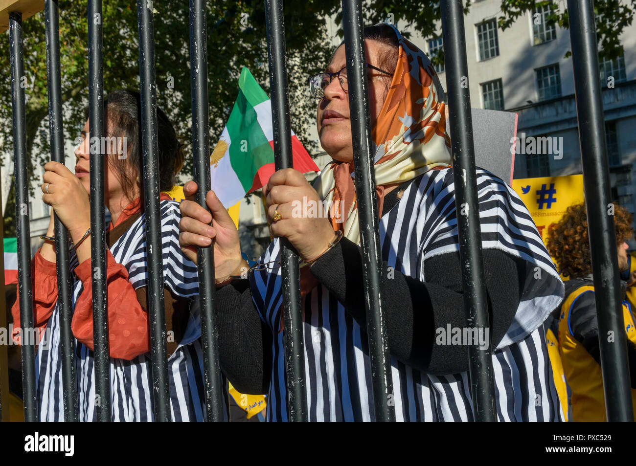 Londra, Regno Unito. 20 ott 2018. Le donne in abito da prioni stand dietro prigione bar alla protesta. Dietro un banner "democrazia in Iran con Maryam Rajavi', Mujaheddin del popolo dell'Iran terrà una manifestazione di protesta contro la repressione del regime attuale in Iran con un patibolo e tre donne detenute in una cella di prigione che illustra il regno del terrore vi e per chiedere la fine delle esecuzioni ci, . Rajavi, il leader dell'OMPI, ha esposto un 10-punto manifesto chiamando per un moderno sistema giuridico, la parità tra i sessi un credito: ZUMA Press, Inc./Alamy Live News Foto Stock