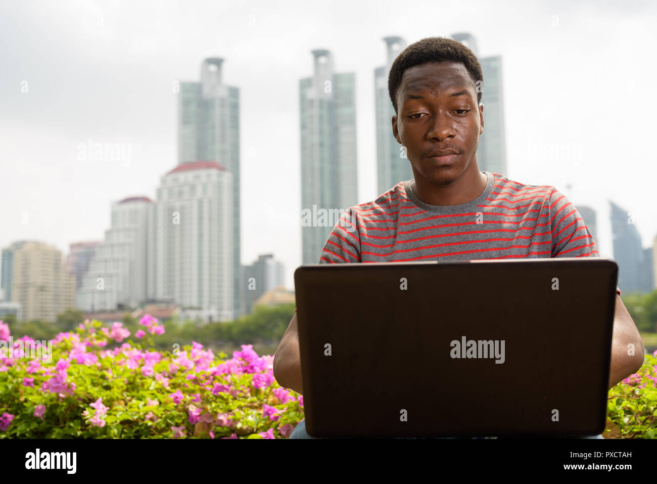 Bel giovane uomo africano utilizzando il computer portatile in posizione di parcheggio Foto Stock