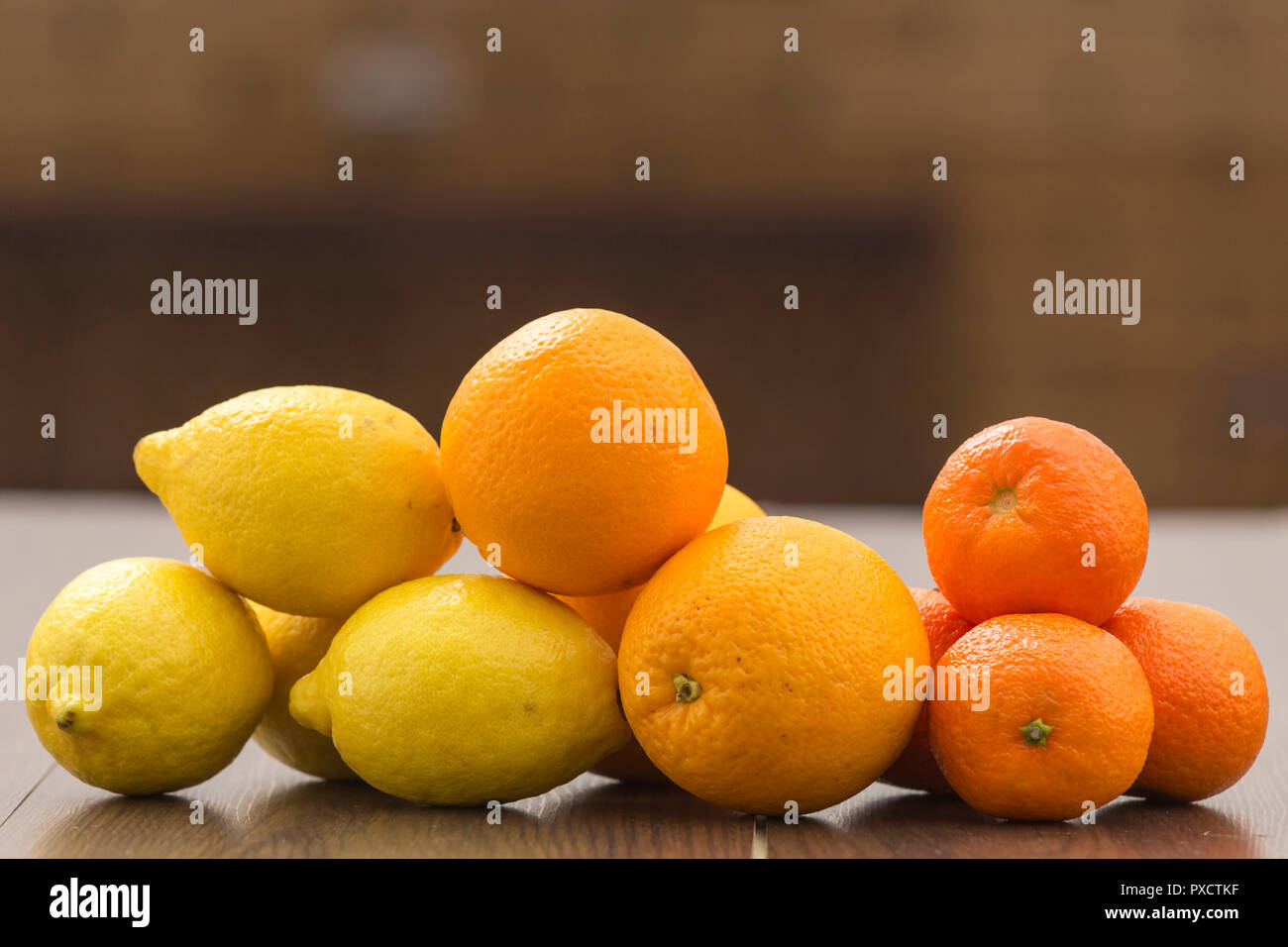 Natura morta con arance, limoni e mandarini messi insieme in gruppi, su uno sfondo e la superficie dei toni di marrone Foto Stock