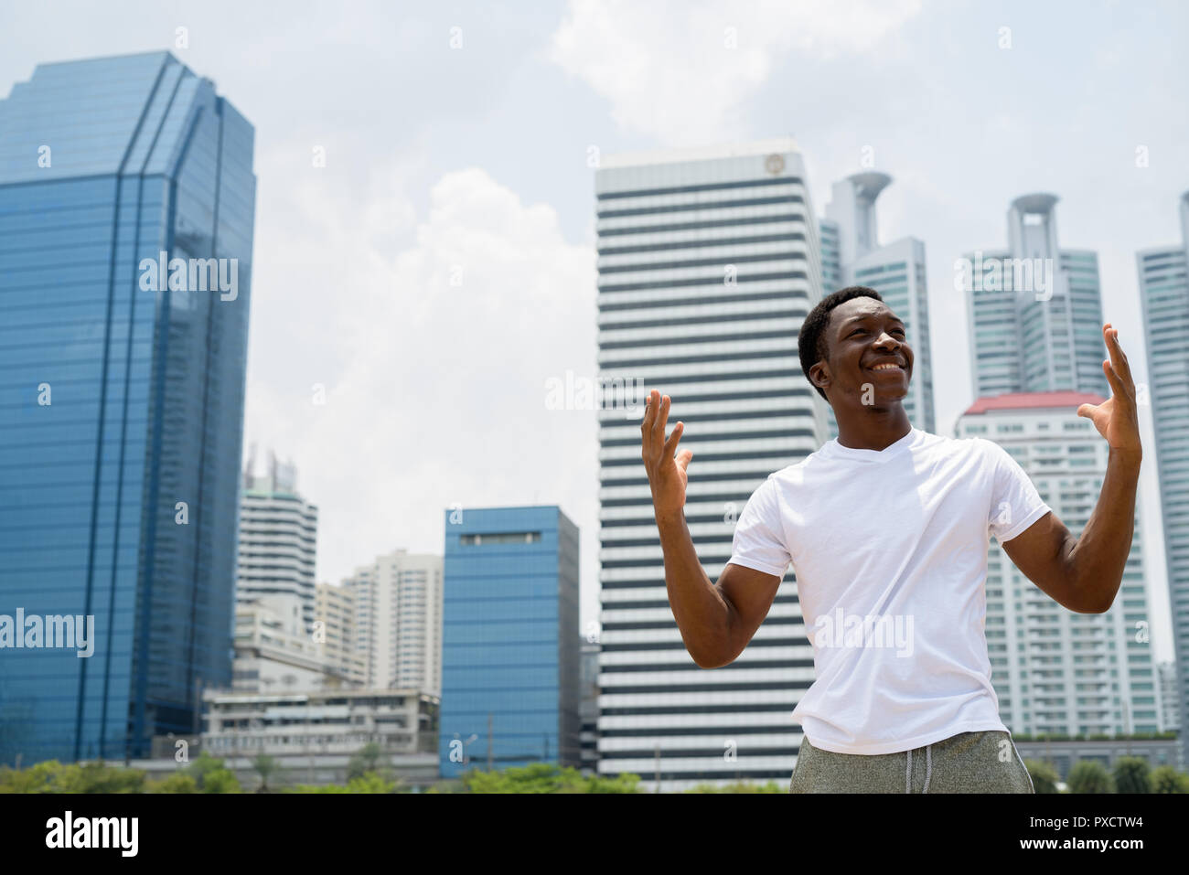 Bel giovane uomo africano con le braccia sollevate all'aperto con il paesaggio sullo sfondo Foto Stock