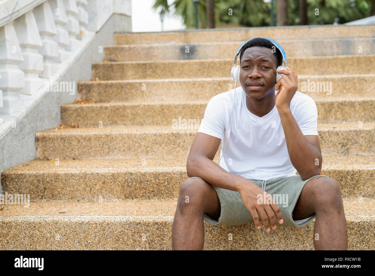 I giovani africani bello uomo seduto sulle scale mentre si ascolta la musica con le cuffie Foto Stock