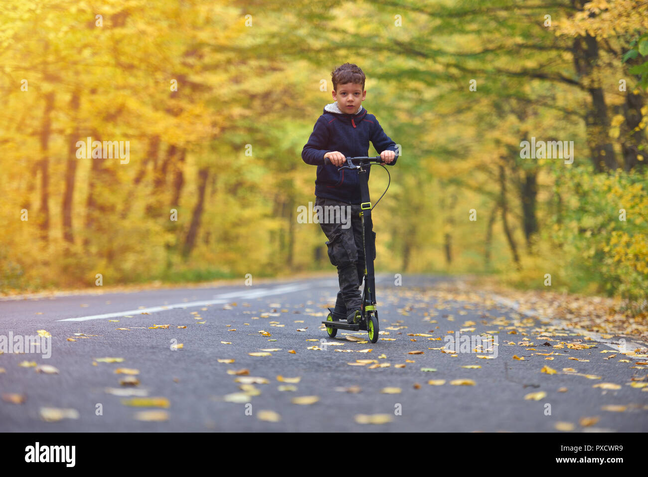 Carino boy riding scooter, outdoor in autunno ambiente sulla sunset luce calda Foto Stock