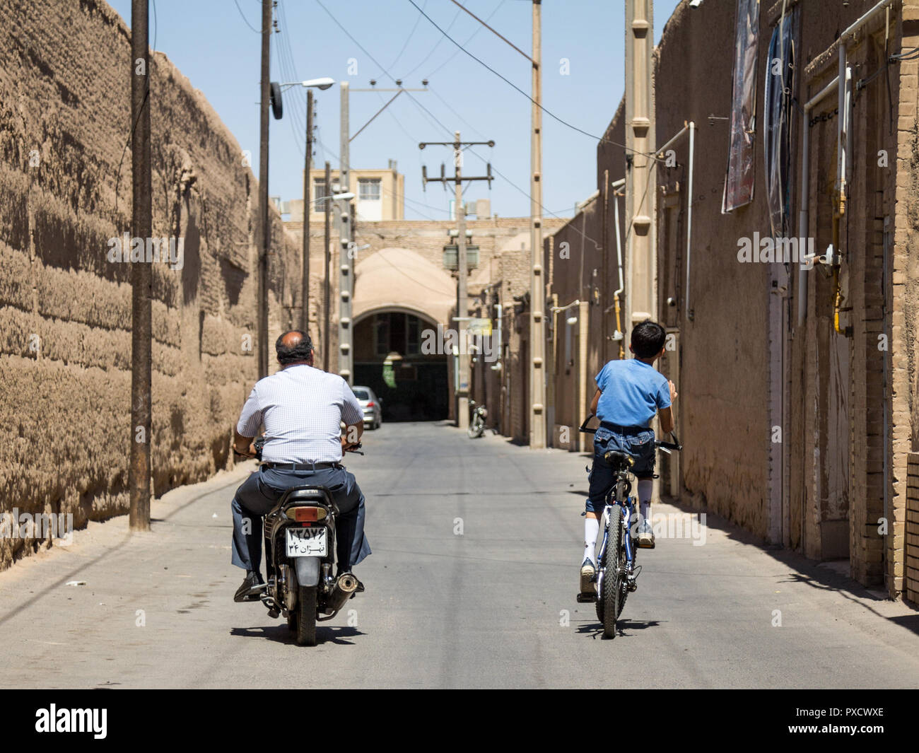 YAZD, IRAN - Agosto 19, 2016: uomo vecchio e giovane ragazzo in sella a una moto e scooter una bicicletta per le strade della vecchia Yazd, la principale città di Central Foto Stock