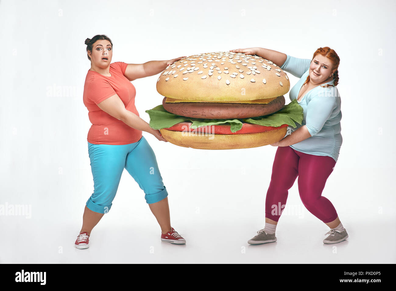 Divertente immagine di divertenti, chubby donne su sfondo bianco. Due donne sono in possesso di un enorme panino Foto Stock