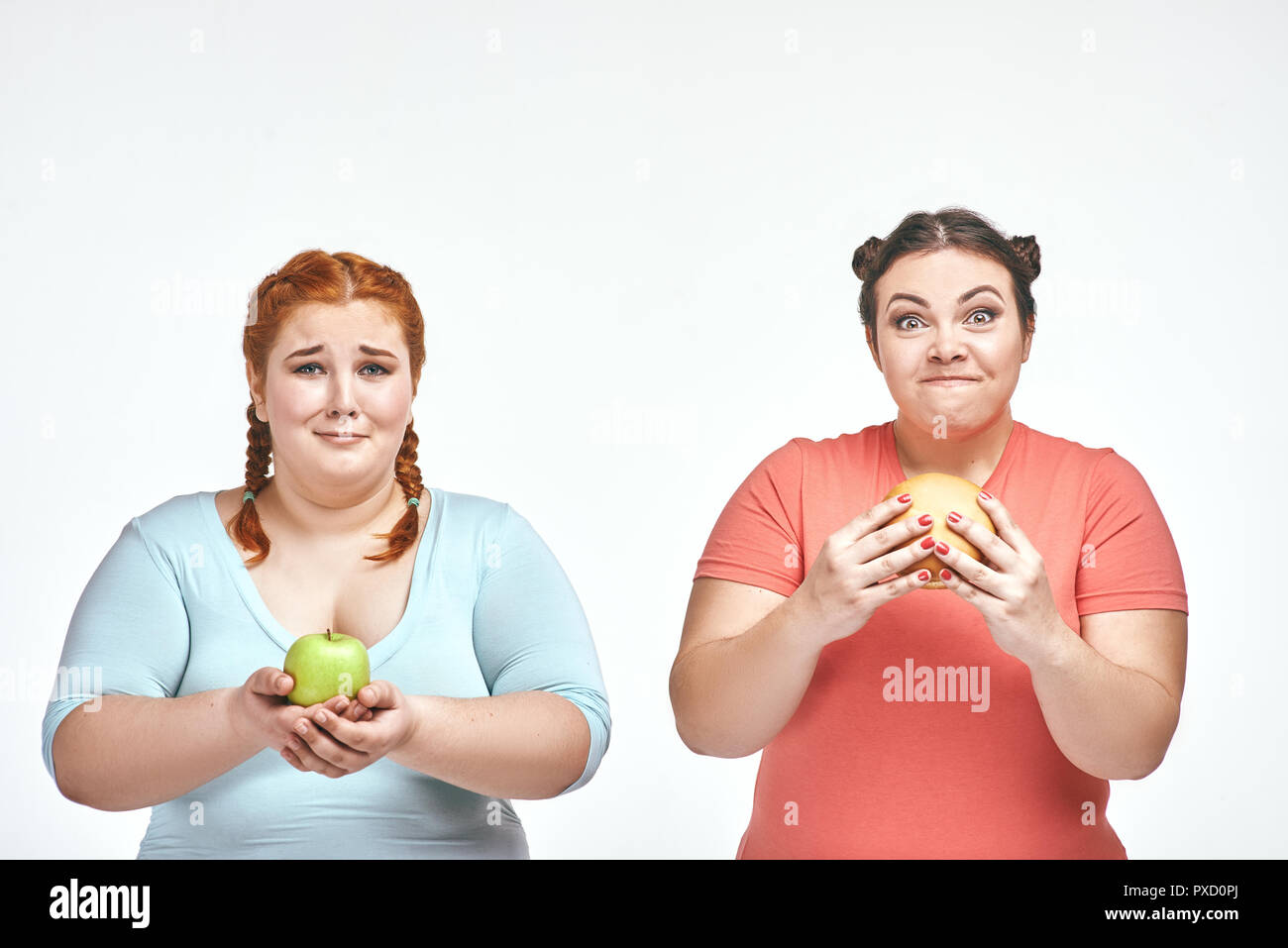 Divertente immagine di divertenti chubby donne su sfondo bianco. Una donna tenendo un sandwich, l'altra azienda un apple. Foto Stock