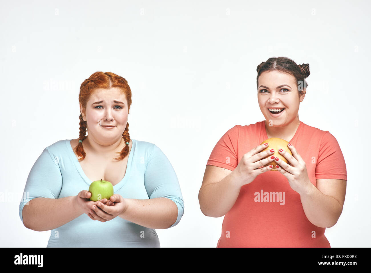 Divertente immagine di divertenti chubby donne su sfondo bianco. Una donna tenendo un sandwich, l'altra azienda un apple. Foto Stock