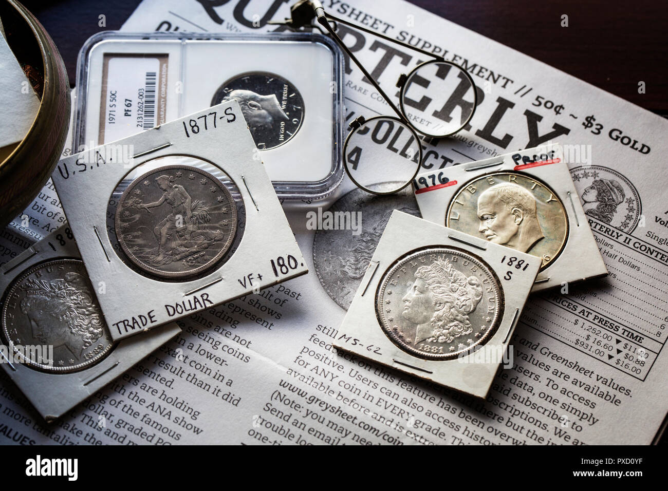 Numismatica - varie monete - Morgan dollari - Dollaro Ike - Commercio - Dollaro contro sfondo del Graysheet con lenti di ingrandimento Foto Stock