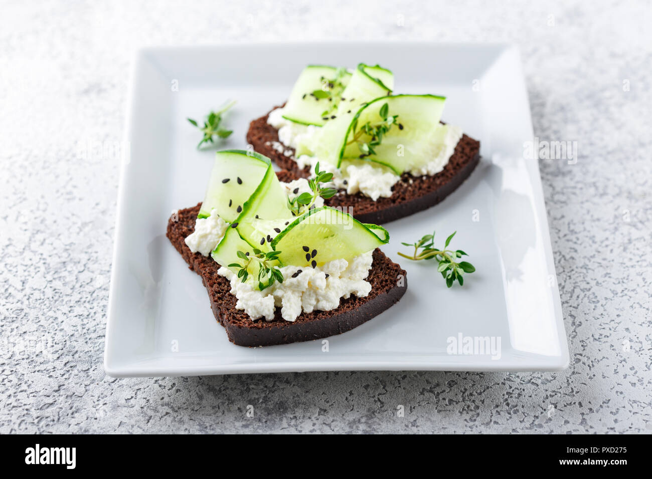 Crostini di pane di segale con ricotta, cetriolo e sesamo nero su grigio ardesia e pietra o calcestruzzo sfondo. Foto Stock