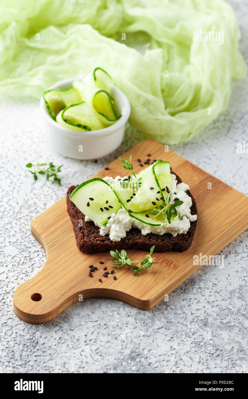 Crostini di pane di segale con ricotta, cetriolo e sesamo nero su grigio ardesia e pietra o calcestruzzo sfondo. Foto Stock