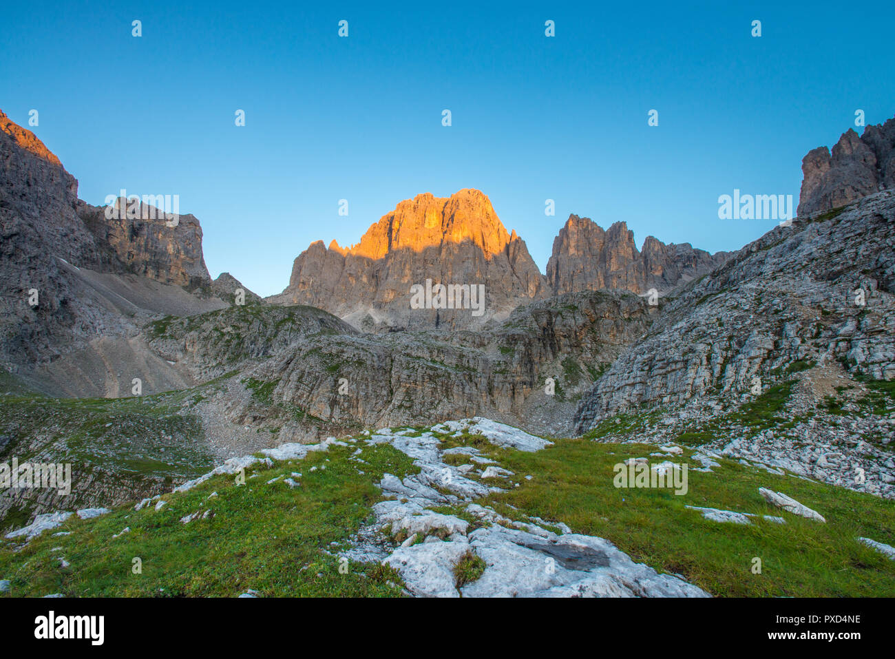 La prima luce del giorno in montagna, incandescente montagna parete in sunrise. Erba, rocce e massi. Cielo blu senza nuvole. Foto Stock