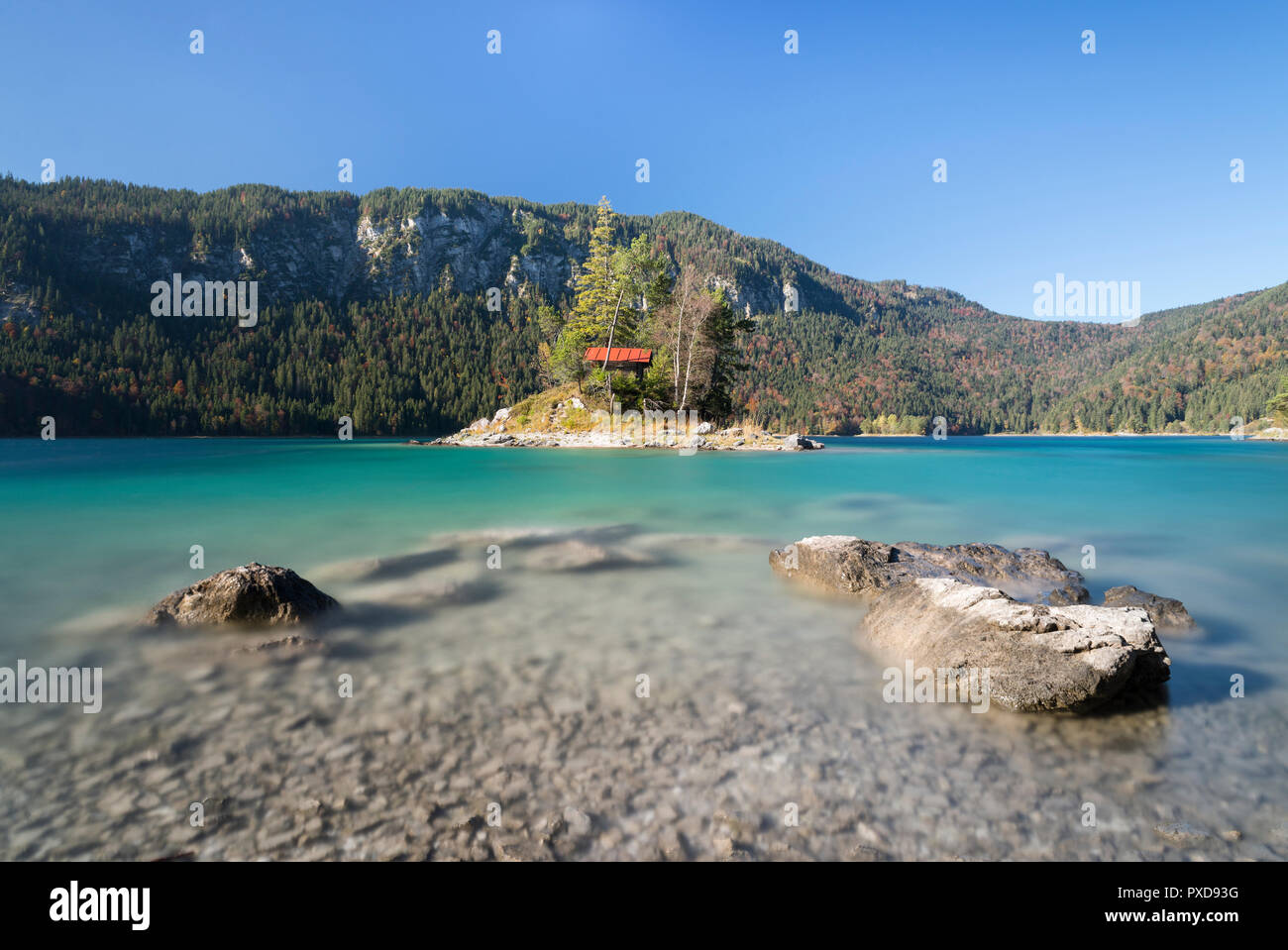 Pietre sulla riva dell'isola Braxninsel davanti al Schönbichl isola nel Lago Eibsee circondato da foresta autunnale, Baviera, Germania Foto Stock