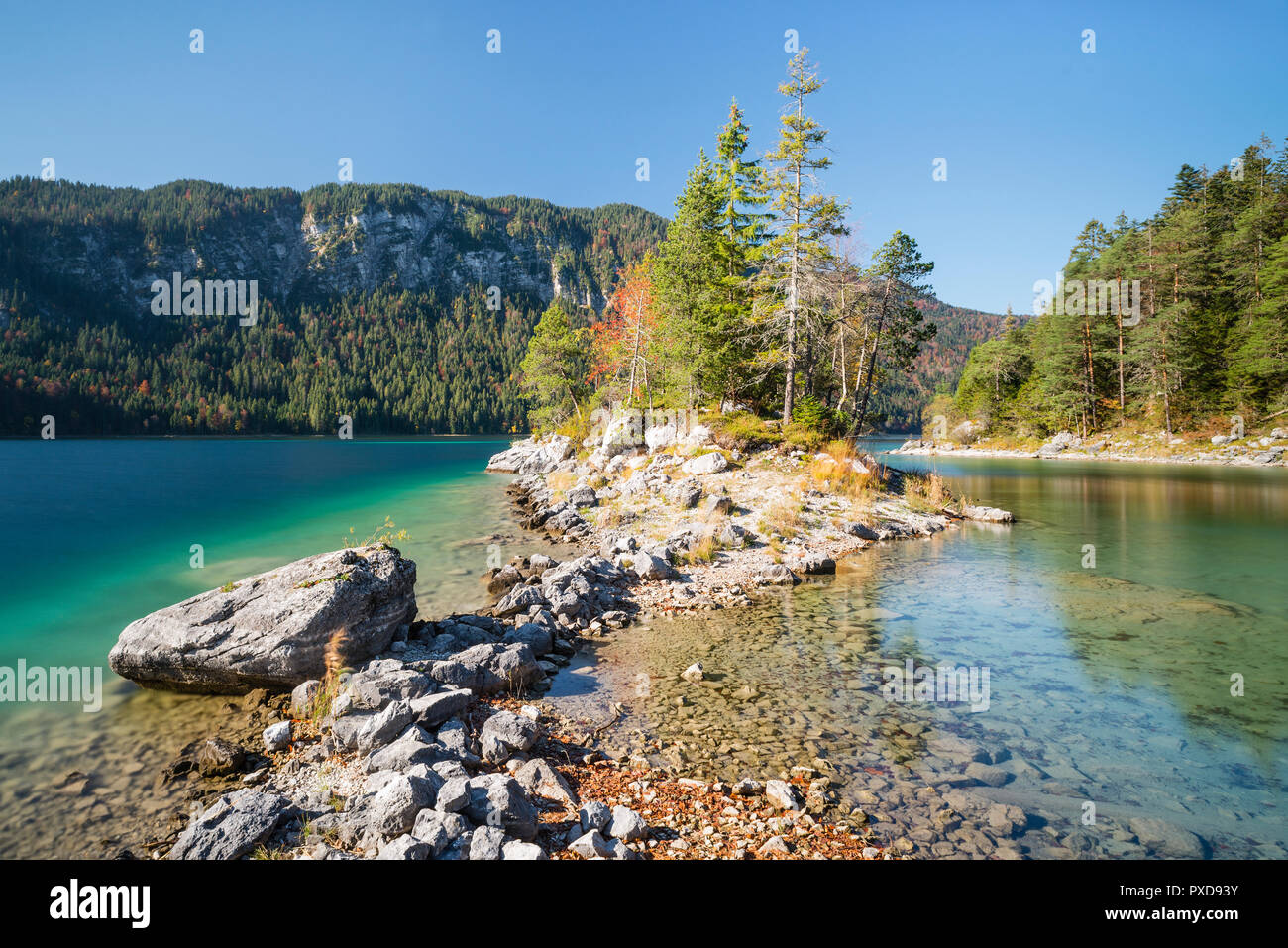 Pietre sulla riva del promontorio oltre a Braxninsel isola nel Lago Eibsee circondato da foresta autunnale, Baviera, Germania Foto Stock
