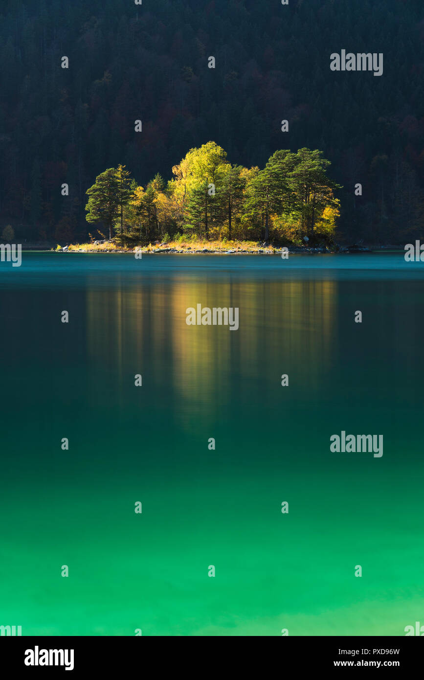 Alberi autunnali risplenda su di Ludwig isola nelle acque turchesi del lago Eibsee nella parte anteriore di un ombroso bosco di montagna, Baviera, Germania Foto Stock
