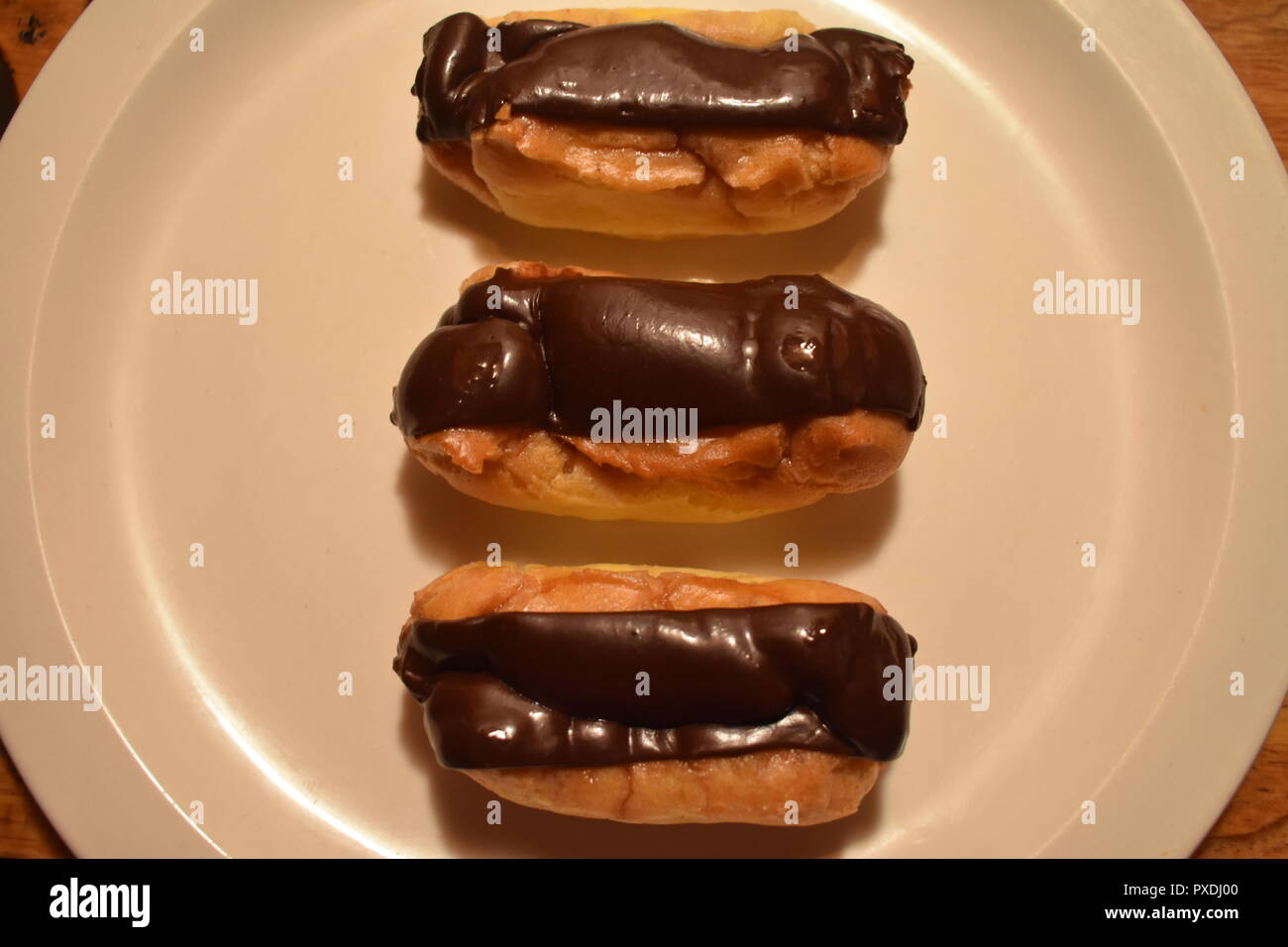 Un delizioso Trio di cioccolato francese Eclair pasticcini serviti su una piastra bianca Foto Stock