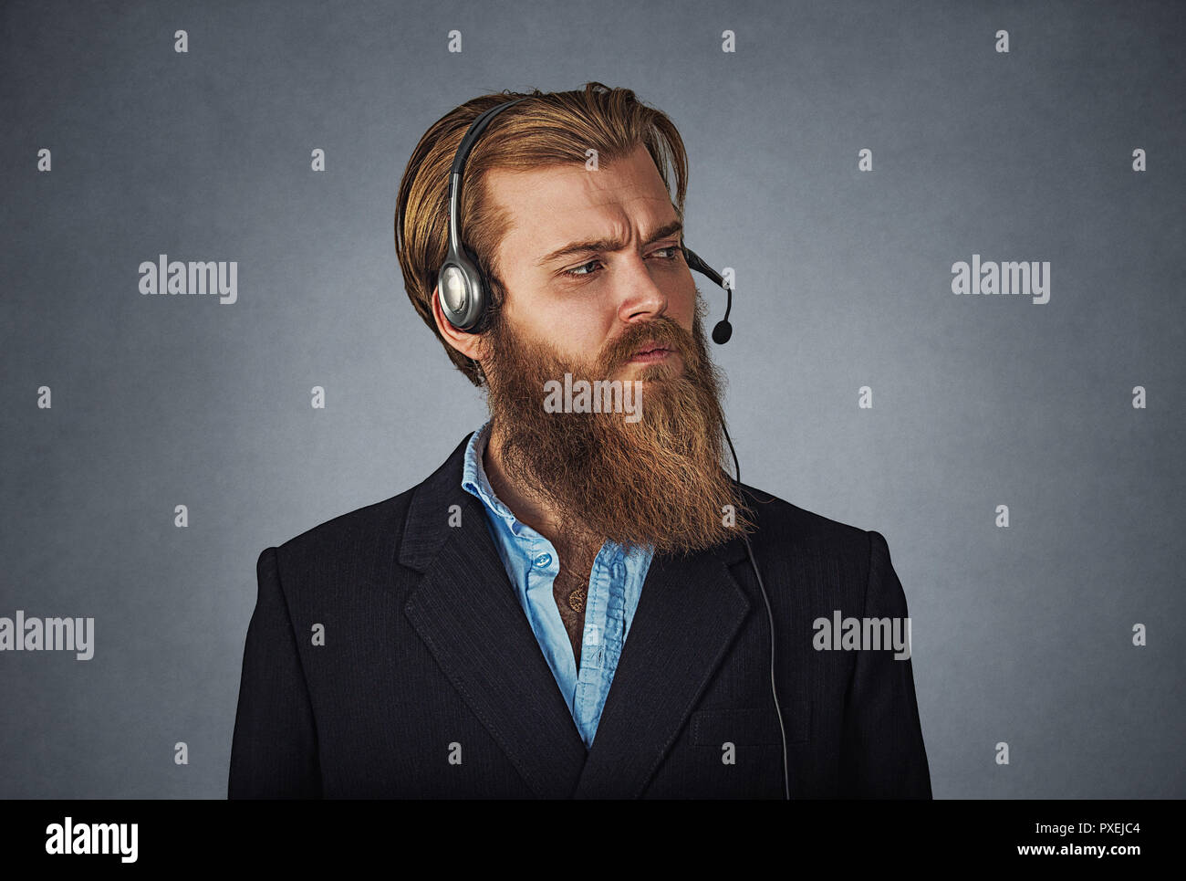 Uomo bello lavorare come un servizio di assistenza clienti, indossa la cuffia alle chiamate, guarda scontroso e annoiato, sconvolto e gravi barbuto hipster business man. Foto Stock