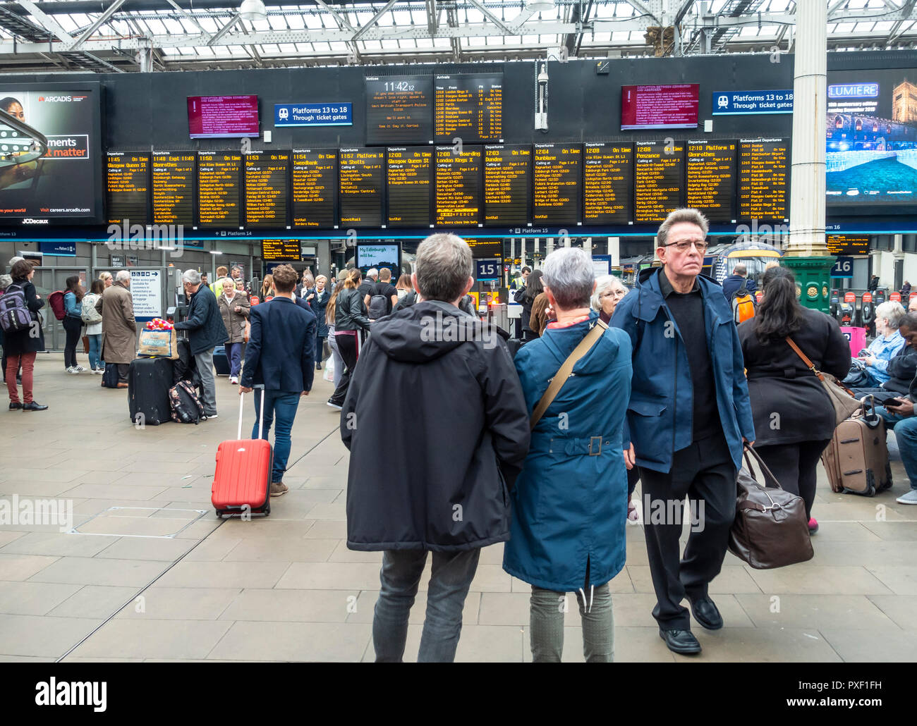 I passeggeri in attesa e arrivati nella parte anteriore delle partenze board presso la stazione ferroviaria di Waverley, Edimburgo, Scozia, Regno Unito Foto Stock