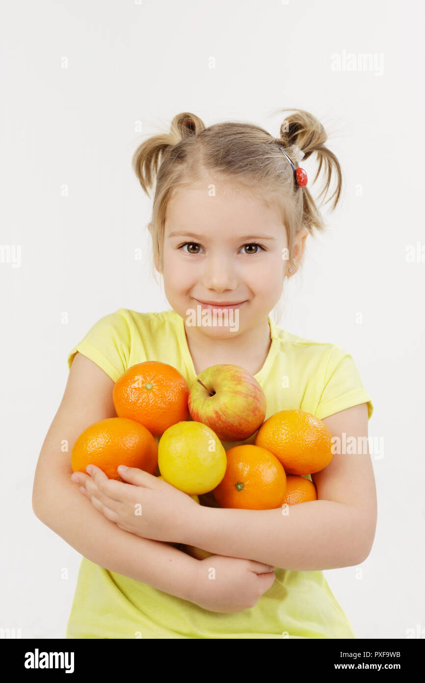 Carino cinque anni ragazza sorridente e azienda frutta - mele, arance e limoni con le sue mani isolato su uno sfondo bianco. Foto Stock