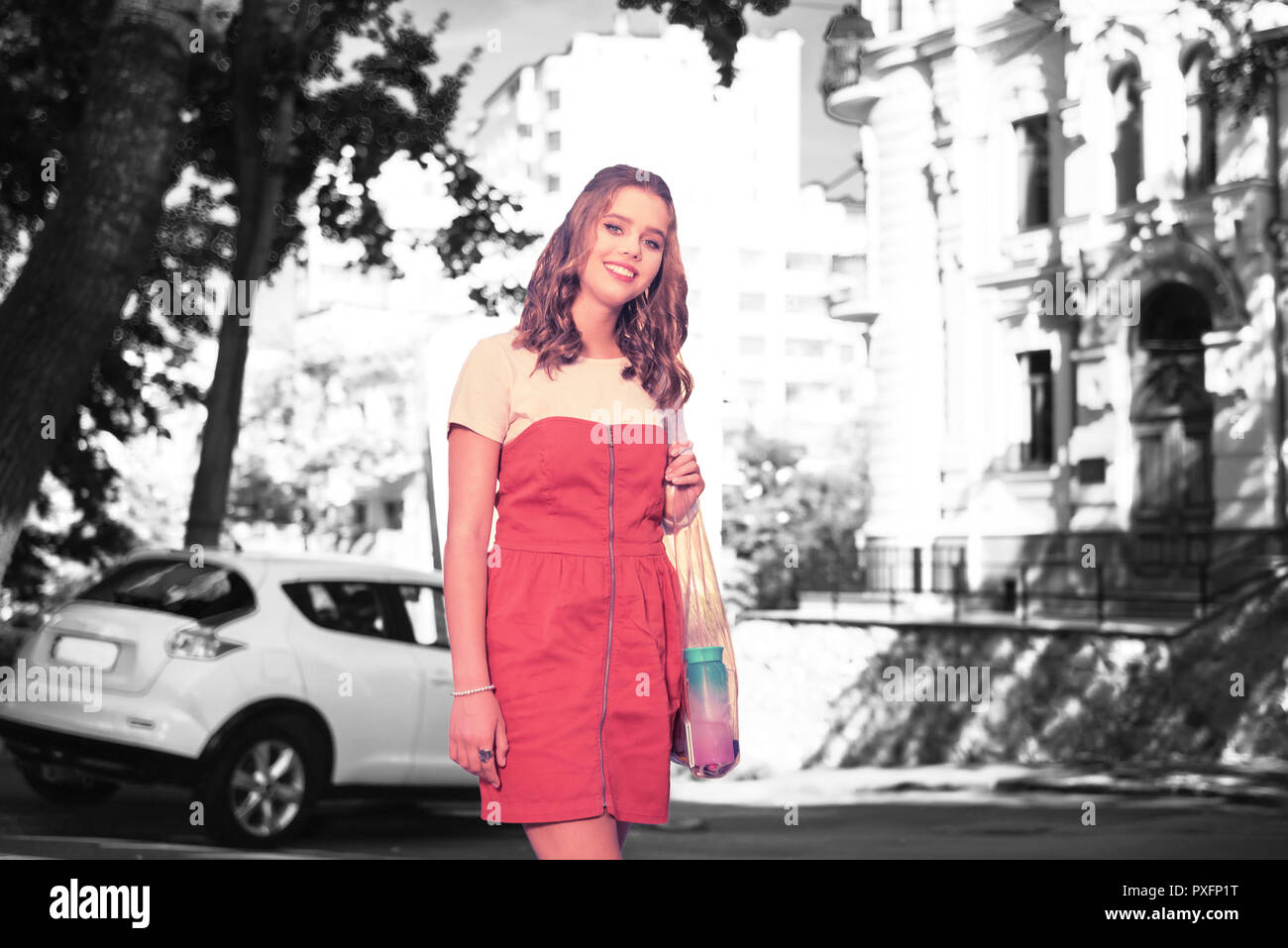 Sorridente attraente giovane donna con trasparente shopping bag in piedi accanto a AUTO Foto Stock