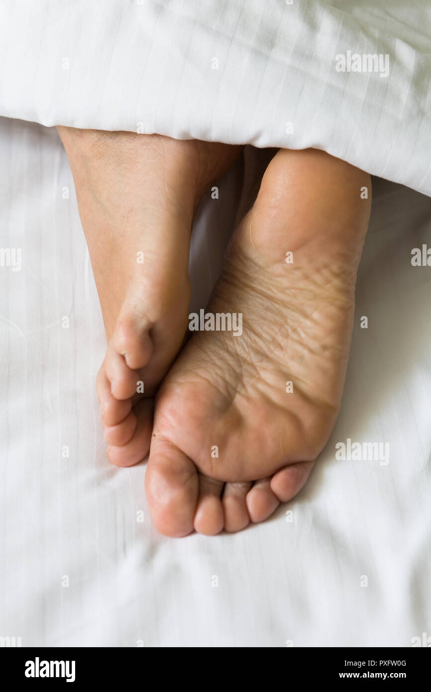 Piedi di gambe umane sporgono da sotto la coperta. Parte del corpo. Foto Stock